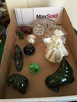Overview of assorted stone carvings, porcelain figurine, crystal clock, and other collectibles laid in box.