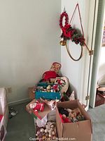 Photo of a corner showing cardboard boxes filled with assorted Christmas ornaments, fabric decorations, and figures.