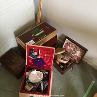 Wide view showing multiple sewing baskets and the Singer sewing machine carrying case on the carpet floor next to a yardstick.