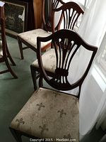 Front view of two shield-back chairs showing carved wooden backrests and upholstered fleur-de-lis seats.