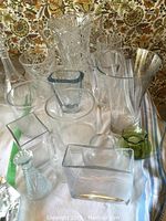Collection of vases in various shapes and clear/green glass on table with floral cloth background
