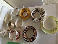 Nine assorted bone china tea cups with matching saucers showing variety of styles and patterns on white surface