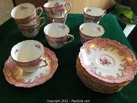 Overall view of 8 stacked pink, gold, floral teacups and matching saucers on green surface.