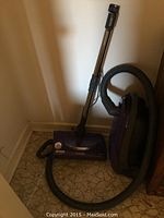 Full view of purple Kenmore vacuum cleaner with hose and metal wand attached, standing against a wall.
