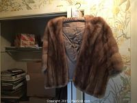 Brown fur shawl hanging on hanger, showing full front and interior lining against wallpaper background.