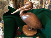 Two wooden pelican carvings placed on green cloth with floral patterned background. One large pelican with wooden base and one smaller pelican figure.