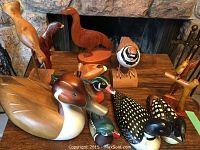 Photo showing a grouping of hand-carved wooden bird sculptures on a stone fireplace hearth, including painted ducks with detailed feathers and natural wood finish birds