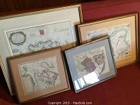 Four framed antique maps showing geographical and historical regions in various framing styles on a red couch.