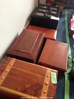 Four wood boxes placed on the floor, three closed including one with brass hardware, one black wood box with glass multi-compartment lid top.