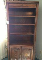 Front view showing three open shelves, two small drawers at the top and double-door cabinet below with brass-colored knobs.