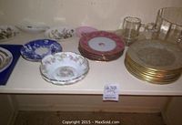 Top view of a variety of plates including Limoges bowl, Crown Derby pink floral plates, Bavaria matching plates, a blue and white plate, and clear glass bowl and mug.