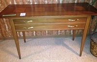 Full front view of the wooden side table showing tapered legs, two drawers with brass handles, and rectangular top surface.