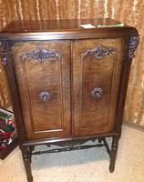 Front view of the walnut finished liquor cabinet with two doors, showing carved floral decorations and turned legs.