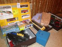 Photo shows the Bachmann HO Electric Train Set in original yellow box including locomotive and freight cars, assorted track pieces nearby, an engineer's hat, and a blue box with accessories.