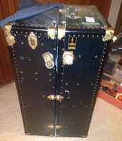 Front view of upright black trunk showing rivets, locks and hinges