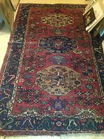 Full view of rectangular wool rug showing red field, navy borders and geometric medallions