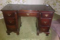 Front view of mahogany finish knee hole desk with glass top protector and brass handles on drawers.