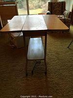 Table open with two drop leaves extended, showing yellow laminate top and chrome legs with wheels in a living room setting.
