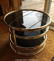 Front view of round brass-framed side table with three smoked glass tiers