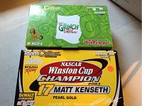 Two unopened boxes shown, one Team Caliber Matt Kenseth 2003 Winston Cup Champion #17 car with pearl gold and DeWalt branding, and one green Grinch-themed NASCAR car box with Kellogg's branding.