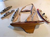 Overview of all five vintage boats on a flat surface: three metal toy warships, one wooden-style plastic yacht with sails, and one white plastic passenger ship.
