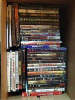 Photo showing stacked DVDs in a box with visible titles on covers, representing the lot assortment.