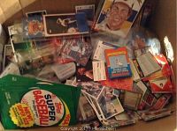 Box containing assorted 1980s baseball cards, sealed Topps pack, and loose cards/spares in sleeves.