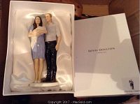 Porcelain figurine set inside white satin-lined box showing a woman holding a baby and a standing man.