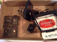 Photo showing all items contained in the lot inside a cardboard box: a Schaefer Beer light sign, two brass mailbox doors, and a black metal train crossing sign.