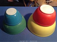Photo of stacked bowls showing red, yellow, green, blue primary colored Pyrex mixing bowls nested together upside down.