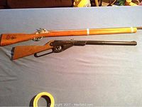 Two vintage wooden toy rifles side by side on a blue cloth. Top rifle is a Disney-themed cap gun rifle with light wood stock and metal barrel. Bottom rifle is a dark wood Daisy lever-action rifle toy gun.