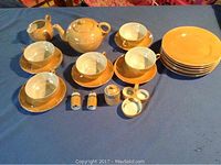 Full set of Japanese luster ware loungeon set including teapot, cups and saucers, plates, salt and pepper shakers, and condiment containers arranged on blue surface