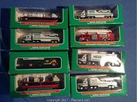 Image shows eight boxed miniature Hess trucks, each labeled with their year and model, including Voyager, Racer Transport, and Electric Fire Truck.