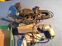 Photo shows four different electrical handheld power tools tangled with cords on a blue surface.
