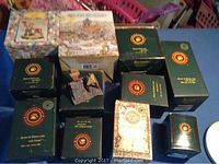 Photo of eleven Boyd's Bears boxed figurines laid out on a table, showing a variety of original green boxes with gold paw print logos, a puzzle box, and some special edition packaging.