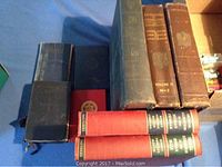 Eight Freemason books arranged flat and stacked on a blue surface, varying sizes and colors indicating collectible first editions