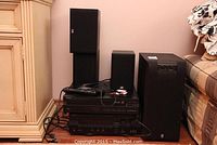 Full view of Yamaha stereo components and speakers on floor near furniture with cables visible. Shows the CD player, receiver, large subwoofer speaker, and smaller speakers.
