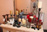 Full view of the lot showing various candles, candlesticks, and holders on a white cabinet with mirror in background.
