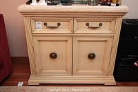 Front view of cream-colored wooden cabinet with stone-like top, two drawers, and two cabinet doors, decorative brass handles.