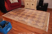 Full view of the carpet placed on wood flooring near a red couch and light-colored cabinet, showing diamond pattern.