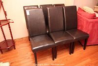 Front view of three dark brown vinyl dining chairs with slight visible damage on one chair seat