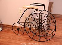 Full side view of the penny farthing decorative piece showing steel wire frame and wood seat against a wooden floor.