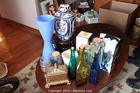Wide view of the decorative lot items on a wooden table, showing oriental urn, glass vases, glass bottles, and ornate brass container.