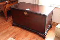 Full view of cedar chest from front angled showing the wood finish, brass keyhole and feet.