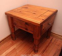 View of one wooden end table showing natural wood grain, square table top with inset panel, drawer with metal knob, and turned legs