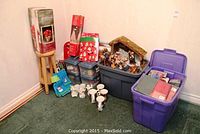 Wide shot showing multiple Christmas decorations including nativity scene, plastic tubs with ribbons and paper, mugs, and gift bags.