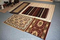 Photo showing all five rugs laid out on floor, with large beige rug in background and smaller rugs in front
