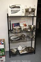 Full view of kitchenware assortment displayed on black metal shelving rack with Franklin Chef rotisserie oven on top shelf and various baking pans and accessories below