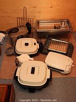 Photo showing the complete lot of small appliances including deep fryer, electric grill, fry pans with lids, kettle, and wire rack.