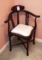 Front view of the dark wooden corner chair with cream fabric seat cushion against a corner wall.